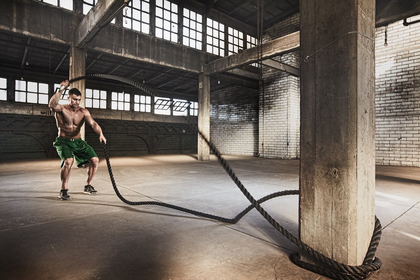 Man exercising with battle ropes in an industrial gym setting for fat burn shaping and fitness.